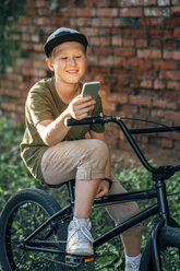 Smiling boy with bmx bike using cell phone - VPIF01206
