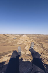 Spain, Navarra, Bardenas Reales, man's legs dangling above meager landscape - RSGF00127