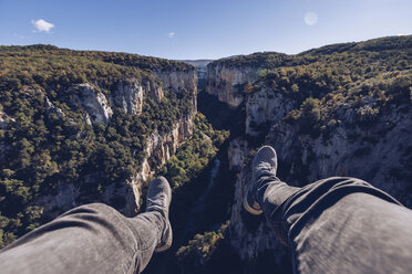 Spain, Navarra, Irati Forest, man's legs dangling above landscape with gorge - RSGF00129