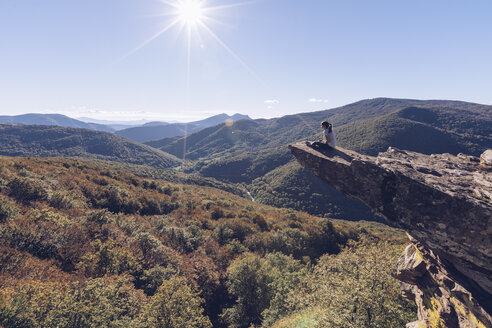 Spanien, Navarra, Wald von Irati, Frau sitzt auf einem Felsvorsprung über einer Waldlandschaft im Gegenlicht - RSGF00140