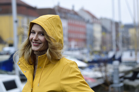 Dänemark, Kopenhagen, Porträt einer glücklichen Frau am Stadthafen bei regnerischem Wetter, lizenzfreies Stockfoto