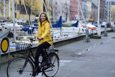 Dänemark, Kopenhagen, glückliche Frau beim Fahrradfahren am Stadthafen bei regnerischem Wetter - ECPF00647