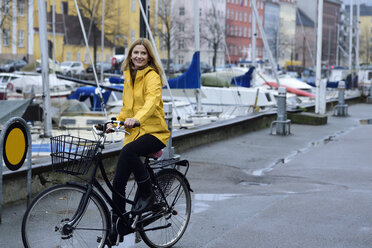 Denmark, Copenhagen, happy woman riding bicycle at city harbour in rainy weather - ECPF00647
