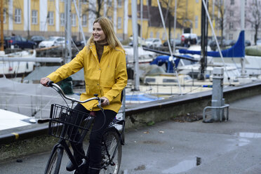 Denmark, Copenhagen, happy woman riding bicycle at city harbour in rainy weather - ECPF00648