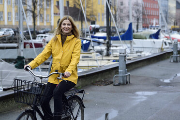 Dänemark, Kopenhagen, glückliche Frau beim Fahrradfahren am Stadthafen bei regnerischem Wetter - ECPF00649