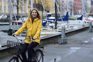 Denmark, Copenhagen, happy woman riding bicycle at city harbour in rainy weather - ECPF00649