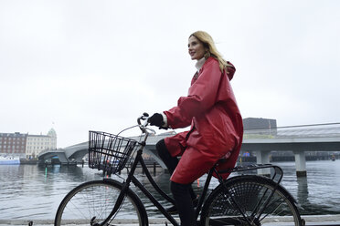 Denmark, Copenhagen, woman riding bicycle at the waterfront in rainy weather - ECPF00663