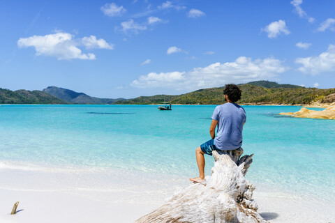 Australien, Queensland, Whitsunday Island, Mann sitzt auf Baumstamm am Whitehaven Beach, lizenzfreies Stockfoto