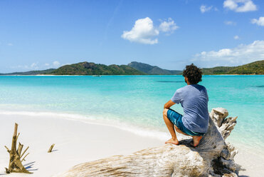 Australia, Queensland, Whitsunday Island, man crouching on log at Whitehaven Beach - KIJF02483