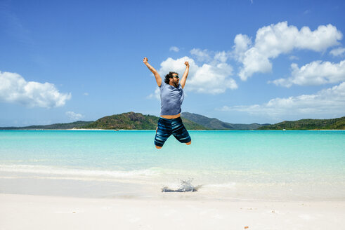 Australia, Queensland, Whitsunday Island, carefree man jumping at Whitehaven Beach - KIJF02486