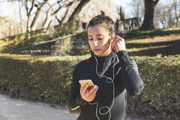 Young woman training and checking her smartphone in park - WPEF01425