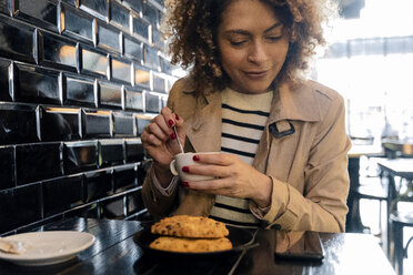 Smiling woman looking at cell phone in a cafe - FMOF00482