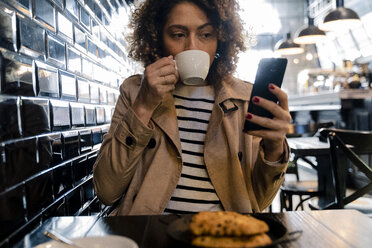 Frau trinkt Kaffee und benutzt ein Handy in einem Café - FMOF00483