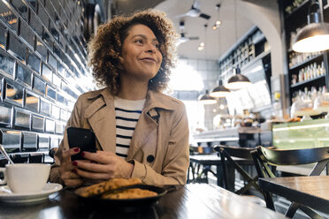 Lächelnde Frau mit Mobiltelefon in einem Cafe - FMOF00485