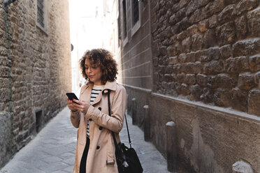 Woman standing in an alley using cell phone - FMOF00488