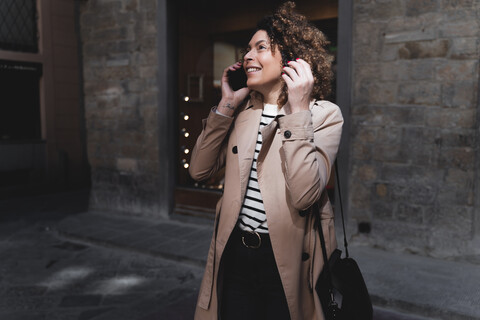 Lächelnde Frau, die in einer Gasse mit einem Handy telefoniert, lizenzfreies Stockfoto