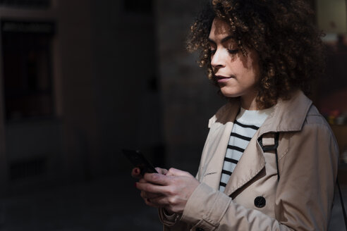 Frau benutzt Mobiltelefon in einer Gasse - FMOF00499