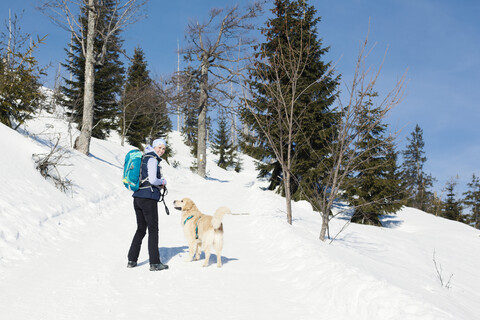 Deutschland, Bayerischer Wald, Lusen, lächelnde Frau mit Hund beim Wandern im Winter, lizenzfreies Stockfoto