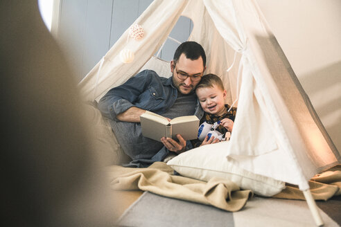 Vater und Sohn lesen gemeinsam ein Buch im Zelt zu Hause - UUF16854