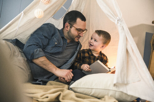 Vater und Sohn lesen gemeinsam ein Buch im Zelt zu Hause - UUF16855