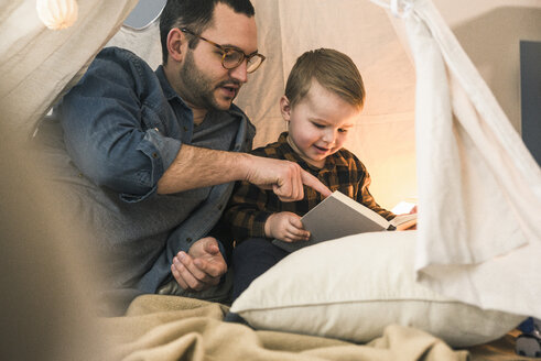 Vater und Sohn lesen gemeinsam ein Buch im Zelt zu Hause - UUF16856