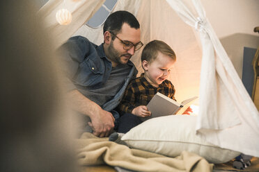 Vater und Sohn lesen gemeinsam ein Buch im Zelt zu Hause - UUF16857