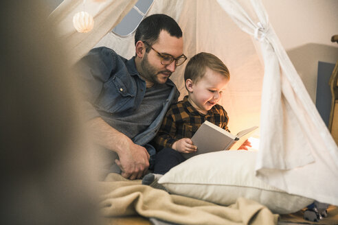 Vater und Sohn lesen gemeinsam ein Buch im Zelt zu Hause - UUF16857