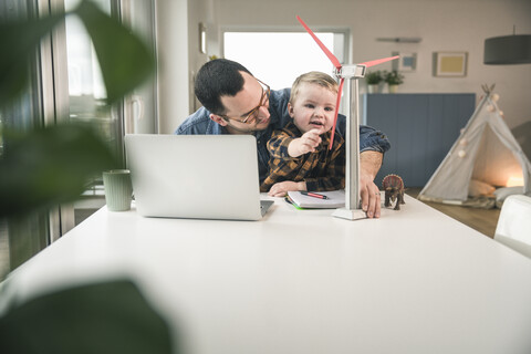 Father and son at home with wind turbine model on table stock photo