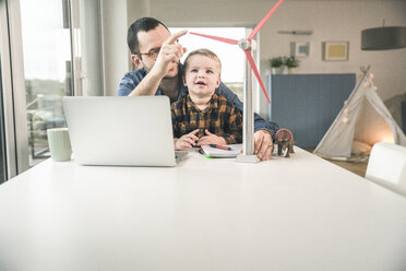 Father and son at home with wind turbine model on table - UUF16866