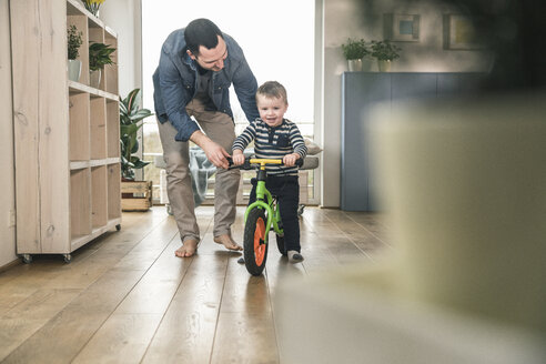 Vater hilft seinem Sohn beim Fahren mit einem Balance-Fahrrad zu Hause - UUF16873
