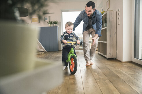 Father helping son riding with a balance bicycle at home - UUF16874