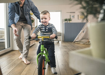 Vater hilft seinem Sohn beim Fahren mit einem Balance-Fahrrad zu Hause - UUF16875