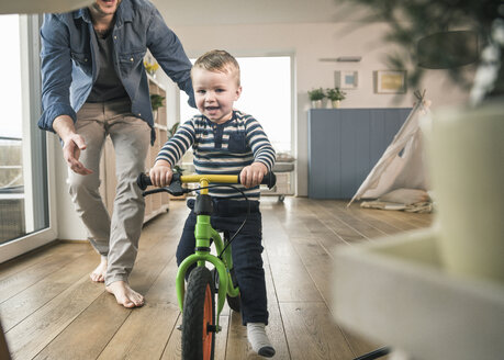 Vater hilft seinem Sohn beim Fahren mit einem Balance-Fahrrad zu Hause - UUF16875