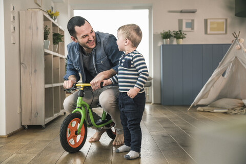 Vater hilft seinem Sohn beim Fahren mit einem Balance-Fahrrad zu Hause, lizenzfreies Stockfoto