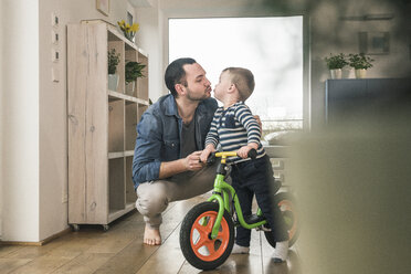 Vater küsst Sohn mit einem Balance-Fahrrad zu Hause - UUF16877