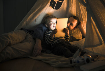 Father and son sharing a tablet in a dark tent at home - UUF16879
