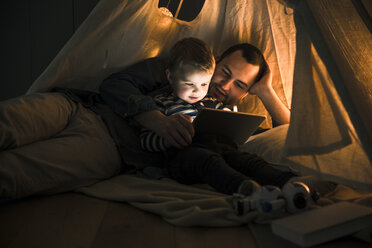 Vater und Sohn teilen sich ein Tablet in einem dunklen Zelt zu Hause - UUF16880