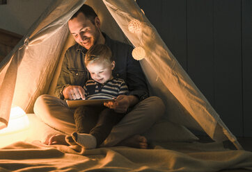 Vater und Sohn teilen sich ein Tablet in einem dunklen Zelt zu Hause - UUF16885