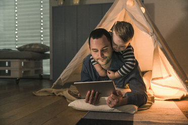 Father and son sharing a tablet at an illuminated tent at home - UUF16888