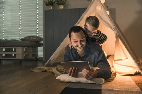 Vater und Sohn teilen sich eine Tafel in einem beleuchteten Zelt zu Hause - UUF16890