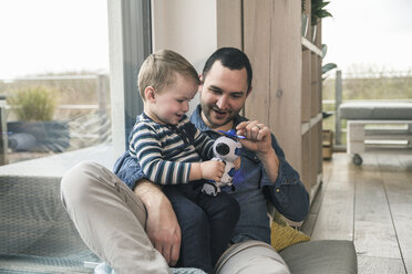 Vater und Sohn spielen mit einem Spielzeugroboter zu Hause - UUF16903