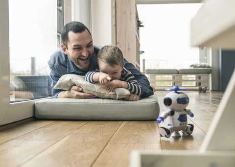 Aufgeregter Vater und Sohn liegen zu Hause auf einer Matratze und beobachten einen Spielzeugroboter, lizenzfreies Stockfoto