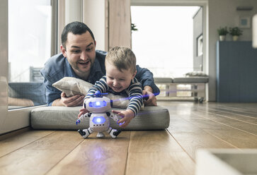 Aufgeregter Vater und Sohn liegen auf einer Matratze zu Hause und spielen mit einem Spielzeugroboter - UUF16910