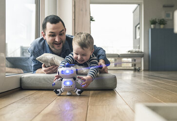 Excited father and son lying on a mattress at home playing with a toy robot - UUF16910