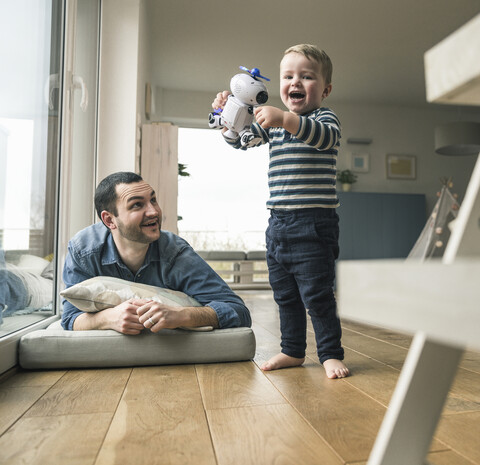 Vater betrachtet aufgeregten Sohn, der einen Spielzeugroboter zu Hause hält, lizenzfreies Stockfoto