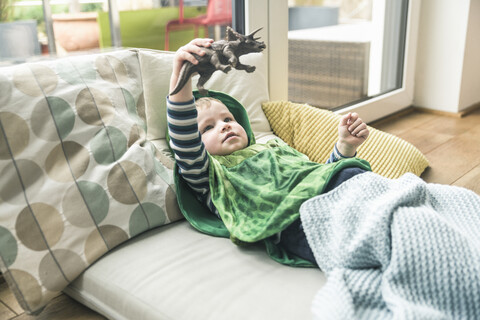 Junge in einem Kostüm auf einer Matratze liegend, der mit einer Spielzeugfigur zu Hause spielt, lizenzfreies Stockfoto