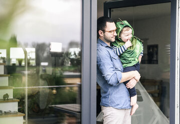 Vater trägt Sohn in einem Kostüm an der Terrassentür zu Hause - UUF16922