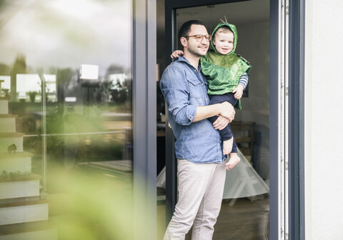 Father carrying son in a costume at terrace door at home stock photo