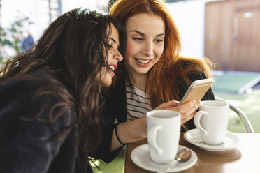 Zwei Frauen schauen in einem Straßencafé auf ihr Mobiltelefon - WPEF01438