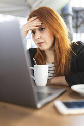 Portrait of redheaded young woman looking at laptop at pavement cafe - WPEF01445